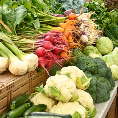 A vibrant display of fresh, locally grown vegetables at a farmers' market, including cauliflower, broccoli, zucchini, onions, and colorful beets. The produce is arranged on crates and tables, emphasizing sustainable, farm-to-table food practices.