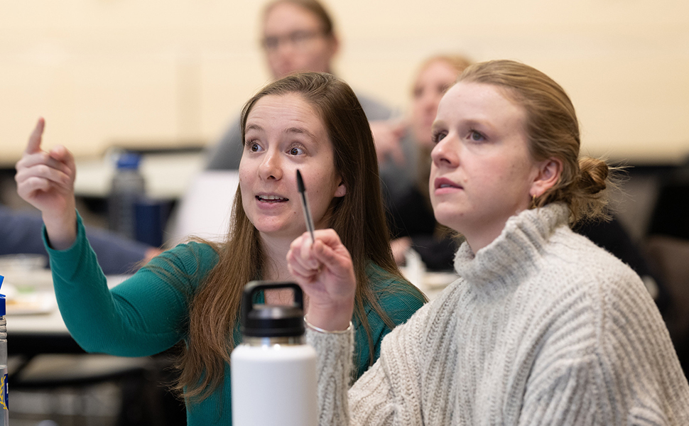 Two women in a classroom looking at and pointing at a screen off-camera