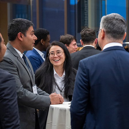 Indian man speaks to group standing around a table as Asian woman smiles at him