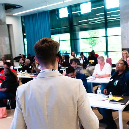 Young white man seen from the back, presenting to a mixed race classrom of adults