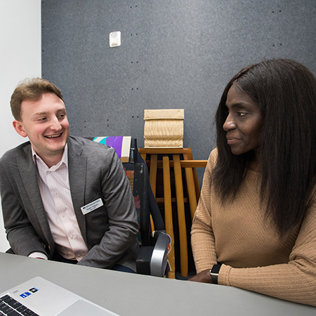 Young white man and older black woman sitting in front of a laptop in an office