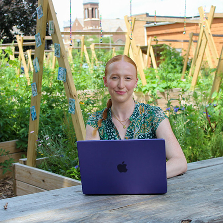 Young redheaded woman sitting at a picnic table in a garden with a laptop in front of her