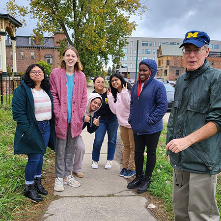 6 female students of diverse backgrounds with older white male teacher on a sidewalk in Detroit