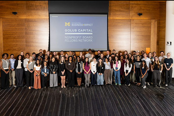 Full Board Fellows Cohort from 2025-26, over 60 students, standing in front of a screen that says Golub Capital Board Fellows