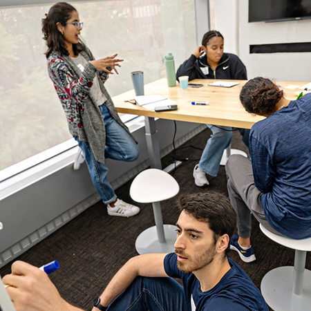 Diverse group of four students working in an Impact Studio pod at a table and on a marker board