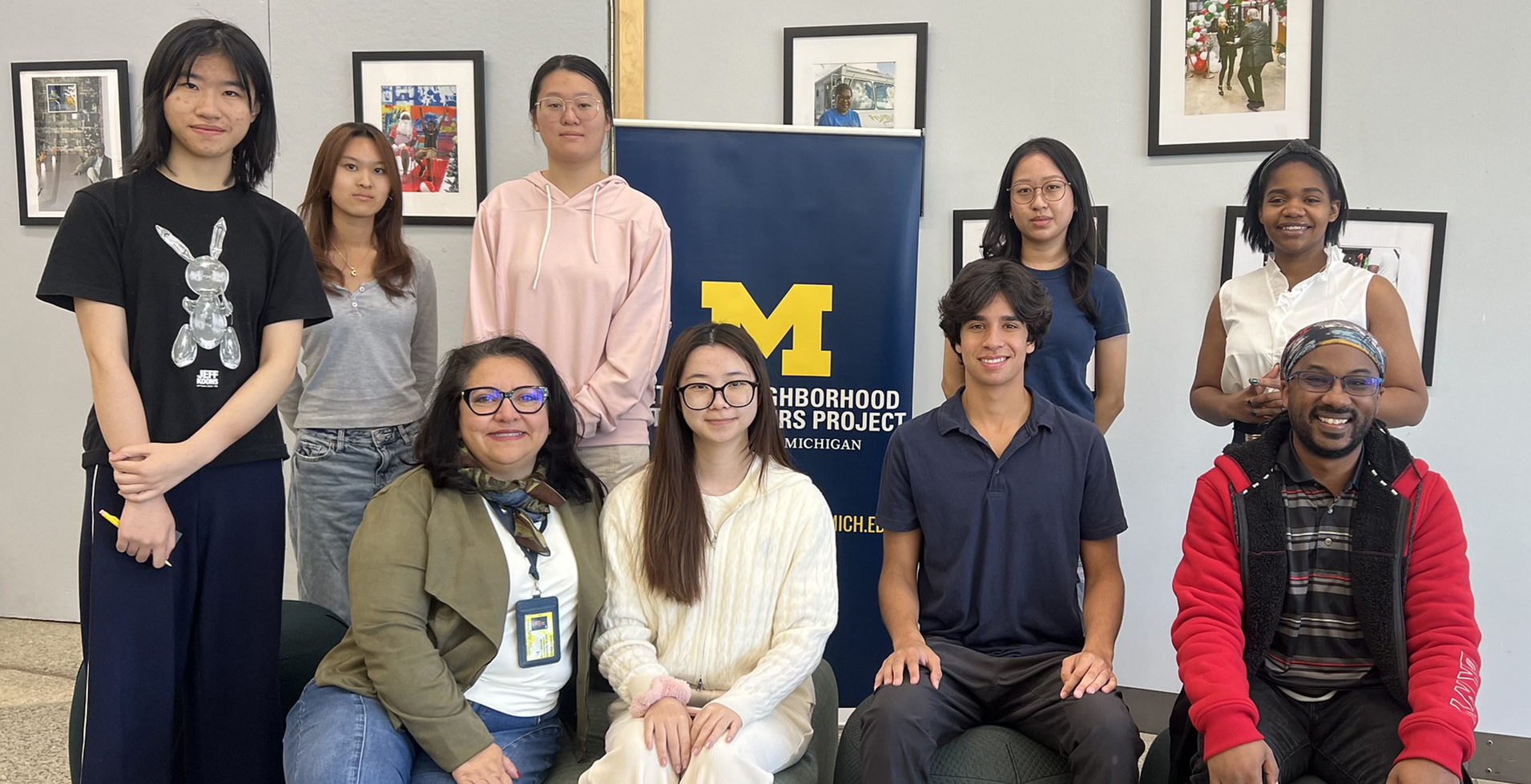 Diverse group of students and an advisor in front of a Detroit Neighborhood Entrepreneurs Project sign