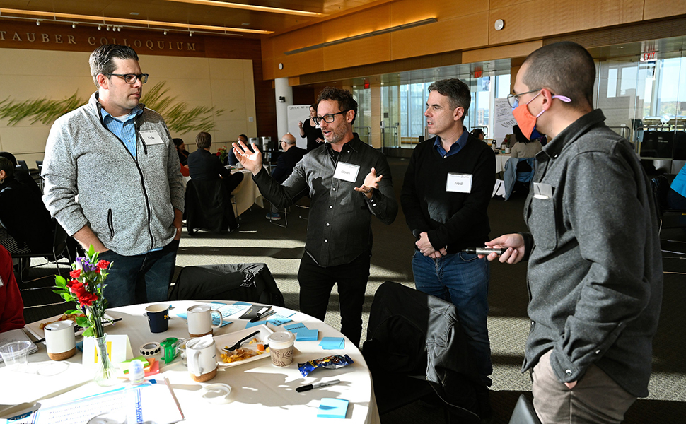 Four men standing in front of table with post-its on it, discussing an idea