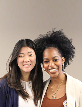 Asian woman and Black woman with heads close together smiling at the camera