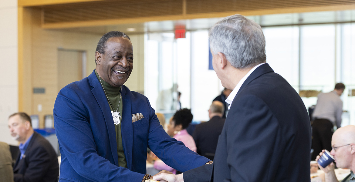 Older Black man shaking hands with an older white man. Both are smiling