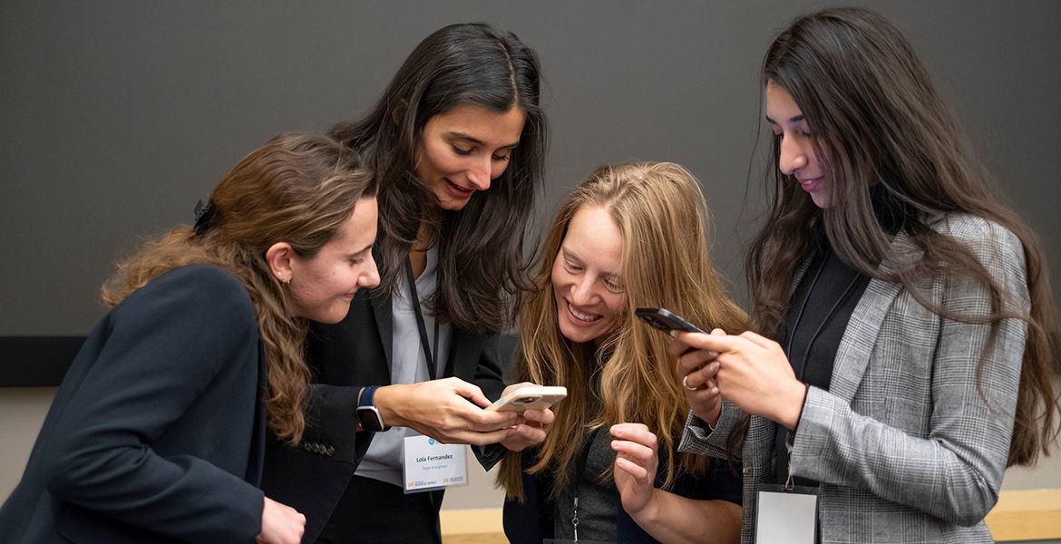 Four female students look at one of their phones and smiling together
